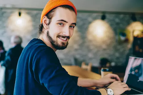 Magenbrennen durch Stress? Lächelnder Mann steht vor Laptop in einem Restaurant.