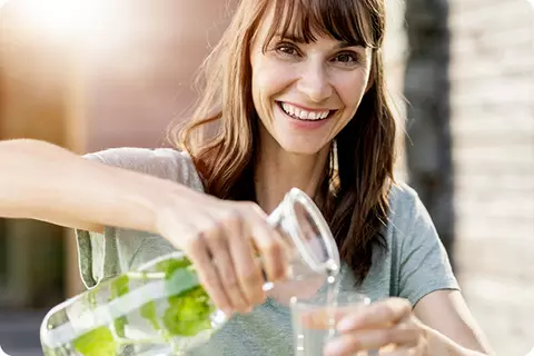 Une jeune femme brune se sert un verre d'eau - Boire suffisamment est important