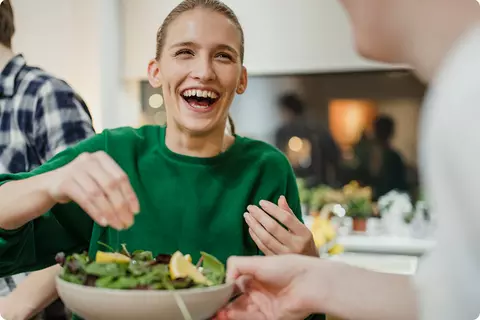 Lachende Frau die sich einen Salat zubereitet - Umstellen der Ernährung
