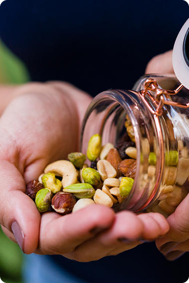 Person schüttet sich aus einem Glasbehälter eine Portion Nüsse in die Hände - Welches Essen lindert Beschwerden?