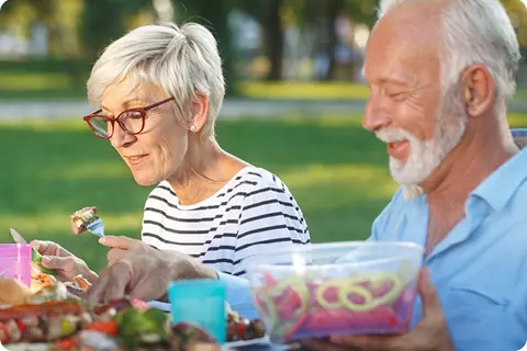 Couple âgé assis confortablement à l'extérieur en train de manger - Manger avec modération peut prévenir les brûlures d'estomac