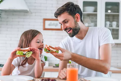 Père et fille sont assis ensemble dans la cuisine et mangent des sandwichs - prendre le temps de manger