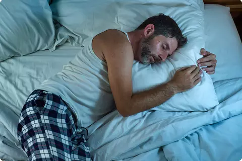 Mann liegt im Bett in Seitenlage auf dem Kissen - Schlafposition optimieren