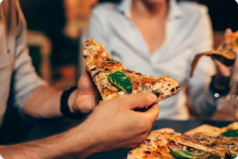 Person hält ein Pizza-Stück in der Hand - Diese Lebensmittel meiden