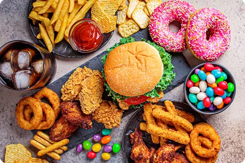 Tisch gefüllt mit ungesundem Essen wie Burger, Donuts, Pommes, Cola - Ungeeignete Lebensmittel
