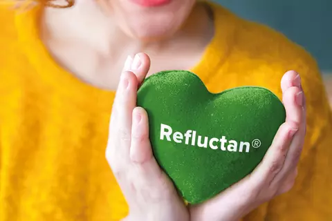 lachende-frau-mit-gelben-pullover-haelt-ein-gruenes-herz-mit-schrift-refluctan