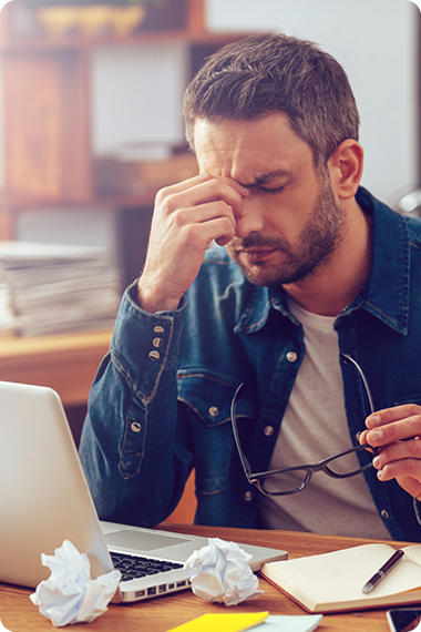 Un jeune homme assis devant son ordinateur portable, les yeux fermés, porte la main à la racine du nez - le stress peut provoquer des problèmes digestifs