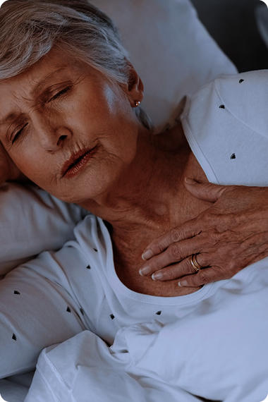 Ältere Frau liegt im Bett und hält eine Hand am Kehlkopf - Wie nächtliches Magenbrennen erkennen?