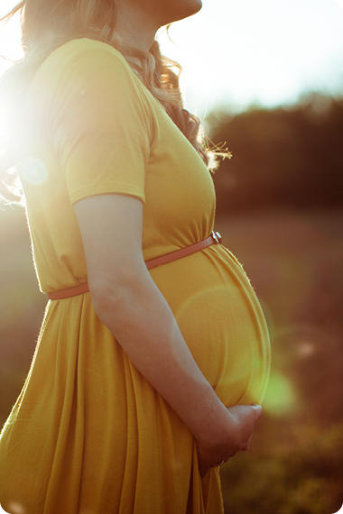 Schwangere Frau im gelben Kleid steht in der Sonne und hält ihren Bauch - Warum haben Schwangere Magenbrennen?