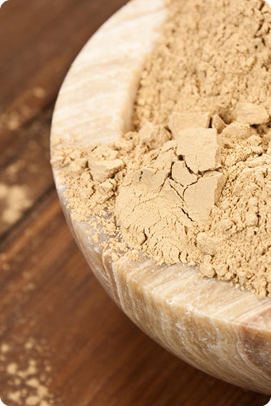 Eine Holzschüssel mit Heilerde auf einem Holztisch - Was bewirken Natron, Backpulver und Heilerde?