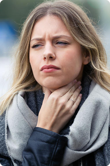 Junge Frau mit blonden Haaren greift sich mit schmerzverzehrtem Blick an den Hals - Reflux