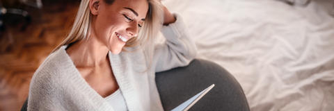 Frau sitzt lachend vor Tablet und macht einen Test - Refluctan Selbsttest Magenbrennen